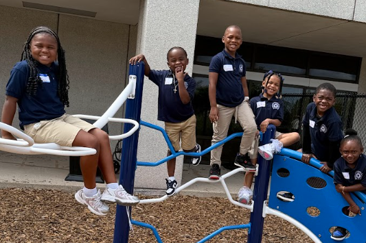 Image of five elementary students in blue polo shirts and khakis playing on a jungle gym.