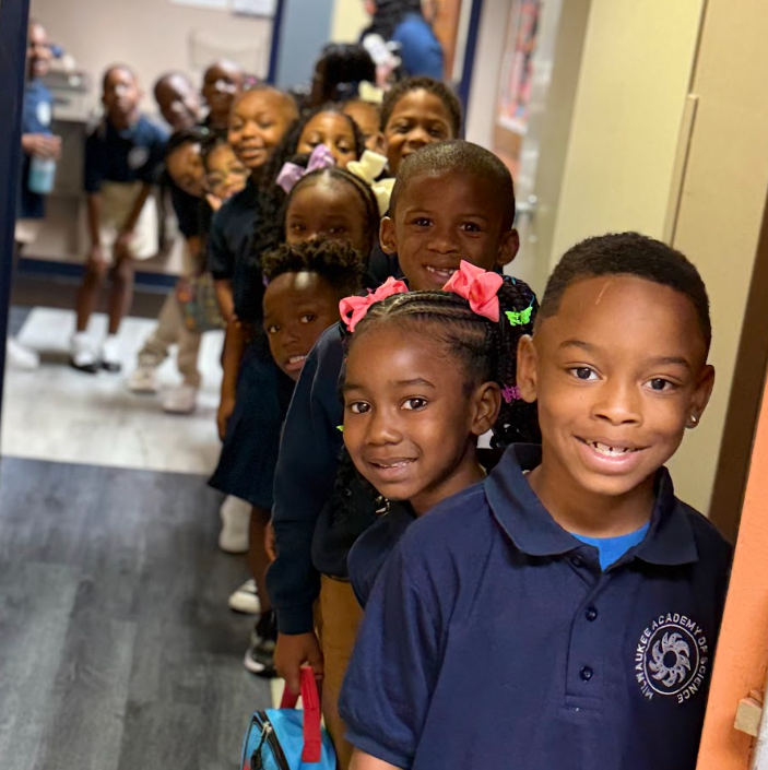 Smiling elementary students in uniforms, standing in a hallway in a single-file line